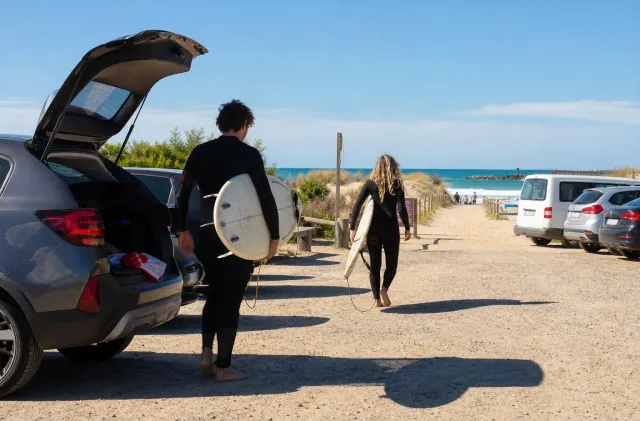 Surfers carrying boards from a Santocha beach car park toward the ocean.