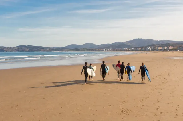 Surf school group walking across Hendaye Grande Plage with the long bay and gentle waves ahead.
