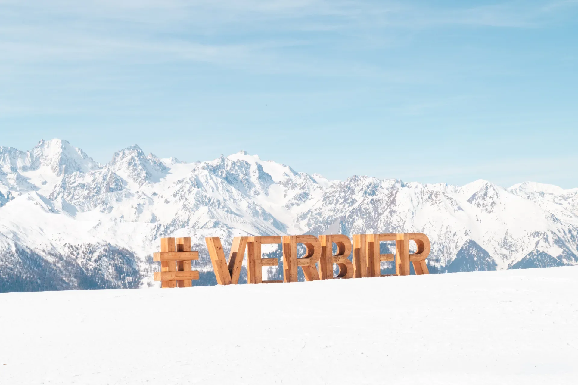 Wooden Verbier resort sign in front of the snow-covered Swiss Alps
