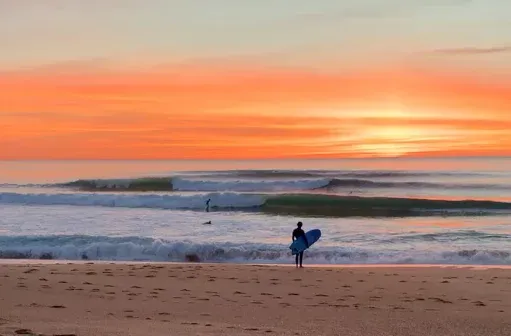 Clean Anglet beachbreak waves at sunset with a surfer on the sand and the Atlantic in view.