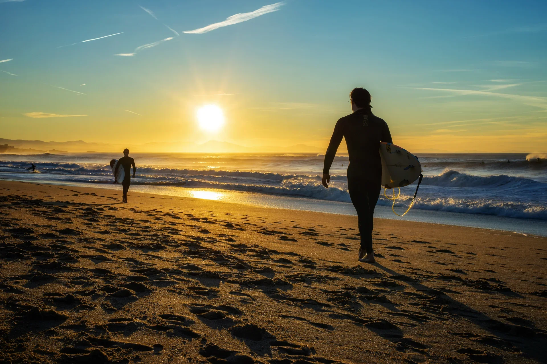 Surfers walking into golden light on an Anglet beach at sunrise