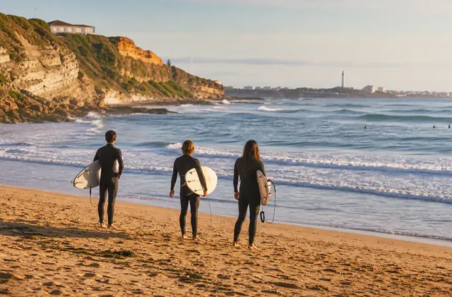 Surfers checking waves at Chambre d'Amour in Anglet with cliffs, beach, and sea in view.